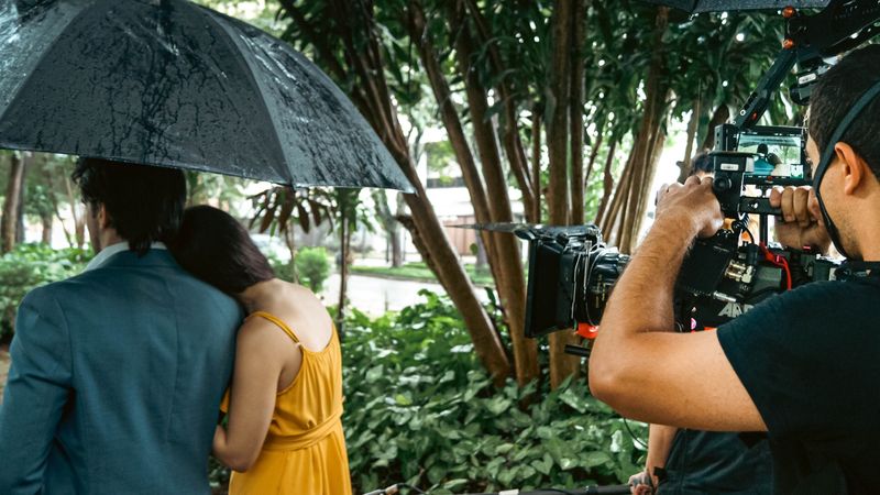 Câmera acompanha um casal sob o guarda-chuva na chuva