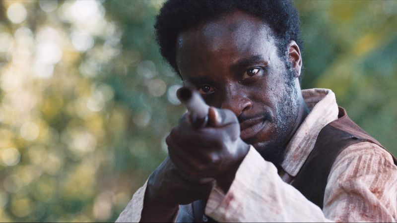 Frame de filme: homem aponta uma arma antiga na mata