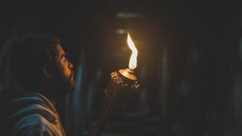Frame de filme: jovem ilumina um corredor escuro com um isqueiro